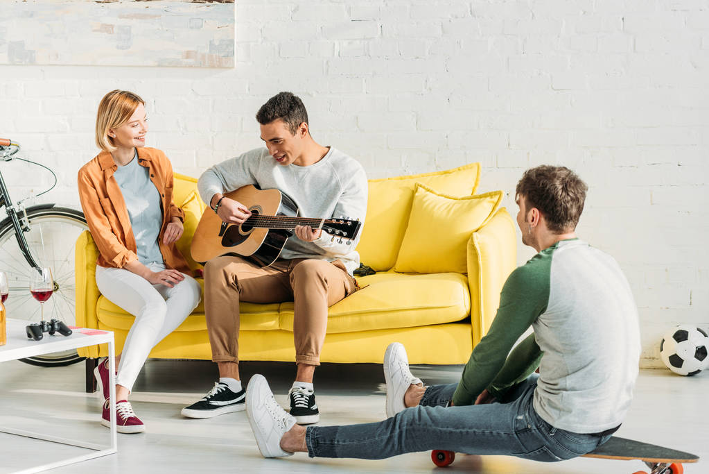 uśmiechnięty mężczyzna mieszanej rasy gry na gitarze dla wielokulturowej przyjaciół w domu - Zdjęcie, obraz