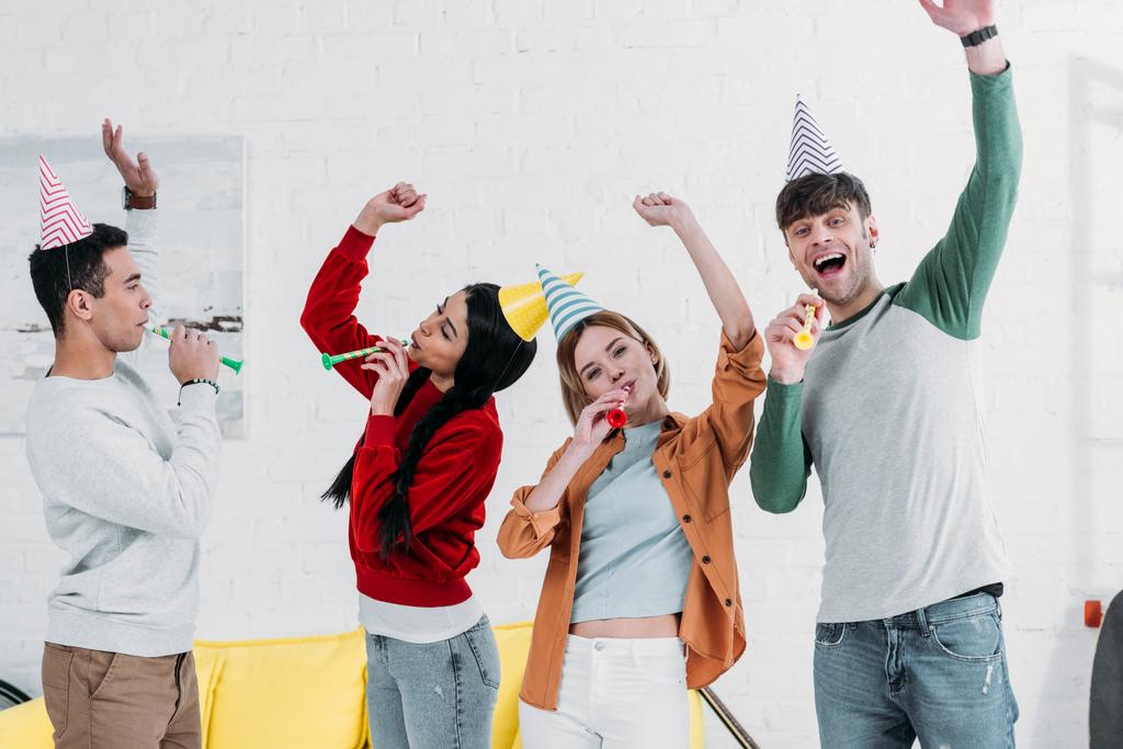 χαρούμενα πολυεθνική φίλοι σε πολύχρωμο χαρτί καπέλα έχοντας διασκέδαση στο σπίτι κόμμα - Φωτογραφία, εικόνα