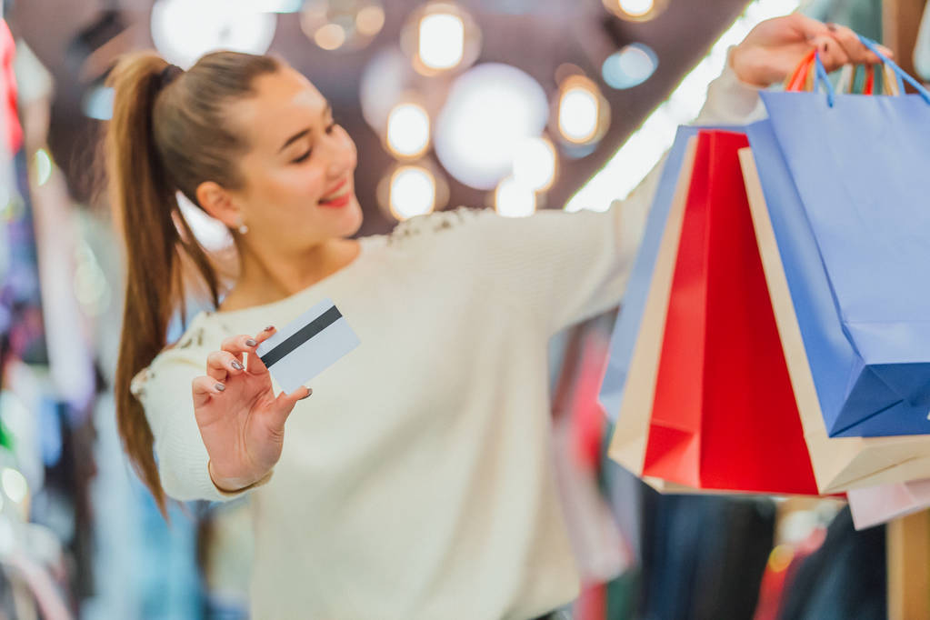 das Mädchen hält eine Kreditkarte und Einkaufstüten mit einem Geschäft. - Foto, Bild