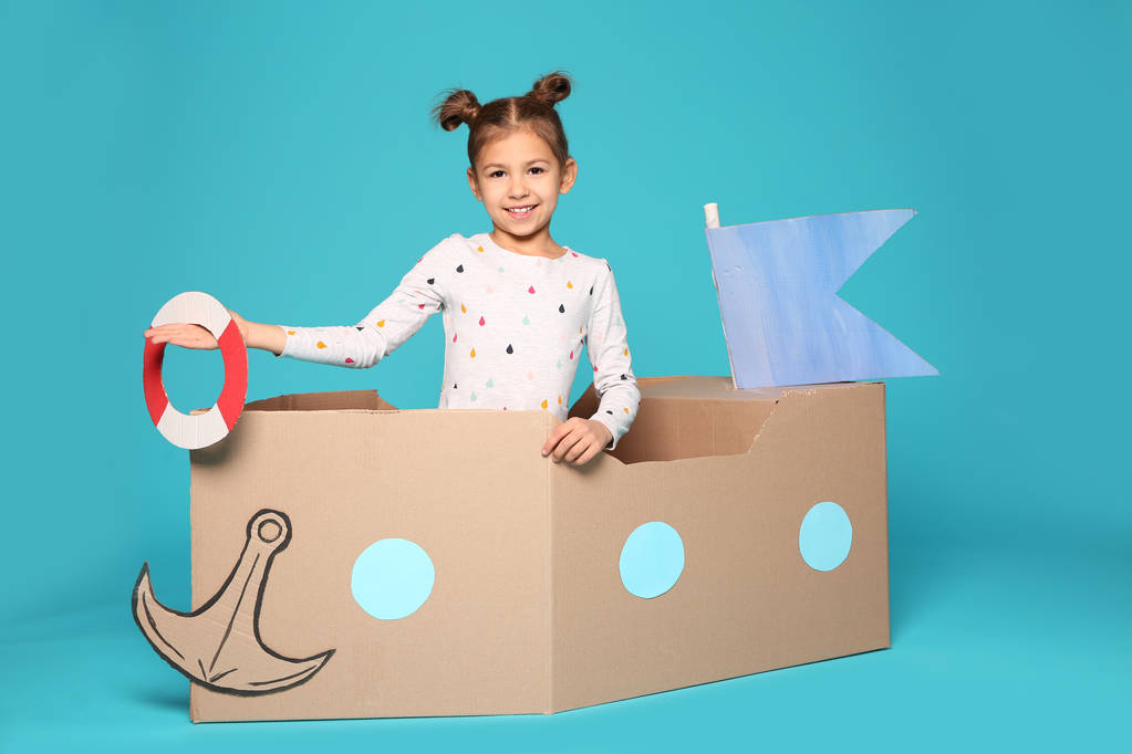 Linda niña jugando con barco de cartón sobre fondo de color
 - Foto, imagen