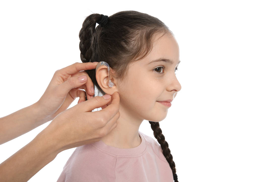 Mujer joven poniendo audífono en la oreja de la niña sobre fondo blanco
 - Foto, Imagen