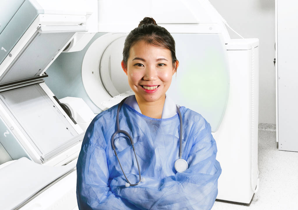 junge glückliche und attraktive asiatische chinesische Medizinerin Ärztin in blauem Peeling lächelt fröhlich im Krankenhaus Scanner-Raum im Gesundheitswesen und erfolgreiche medizinische Karrierekonzept - Foto, Bild