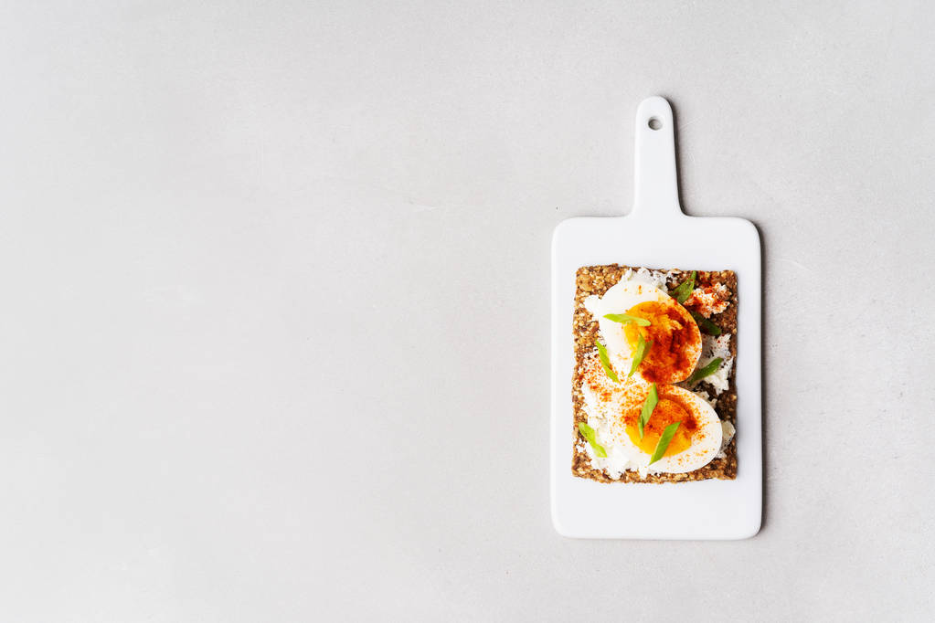 Top view of Superfood protein toast with delicious toppings on top: boiled eggs with onion and paprika on cream cheese lie on ceramic white board. - Photo, Image
