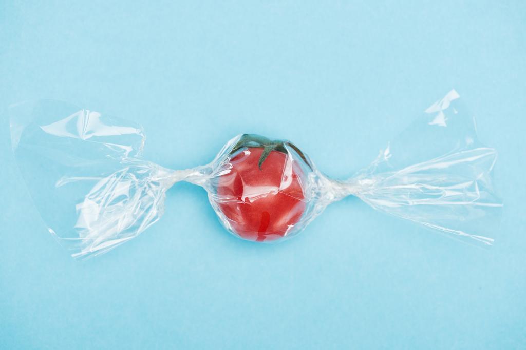 top view of fresh red tomato in transparent candy shaped wrapping on blue background - Photo, Image