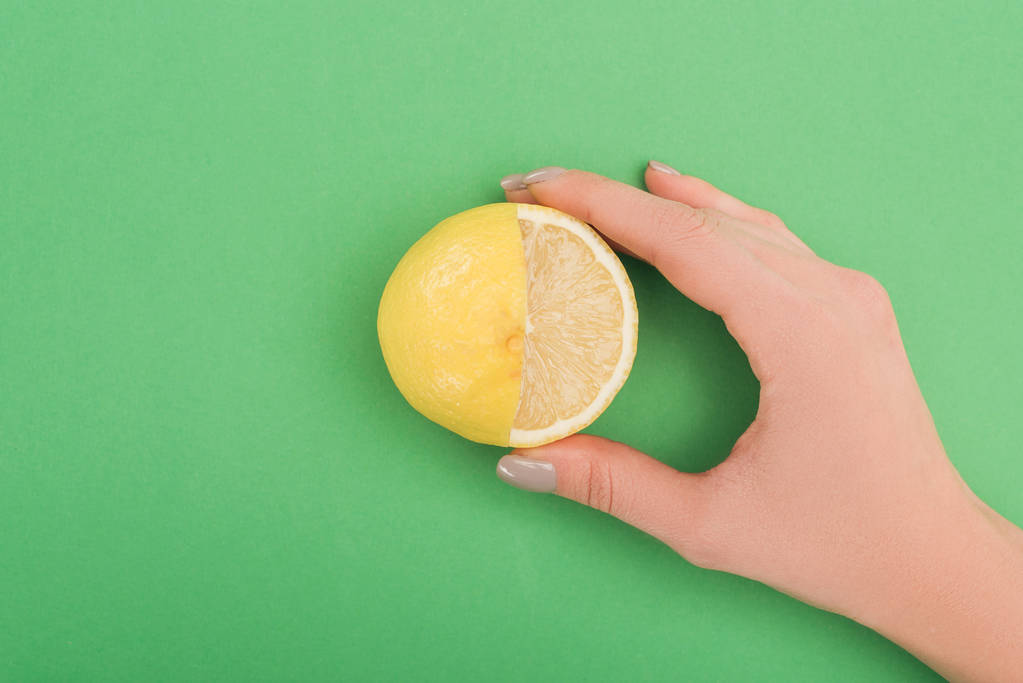 Teilansicht der Frau mit frischer, teilweise geschnittener Zitrone auf grünem Hintergrund - Foto, Bild
