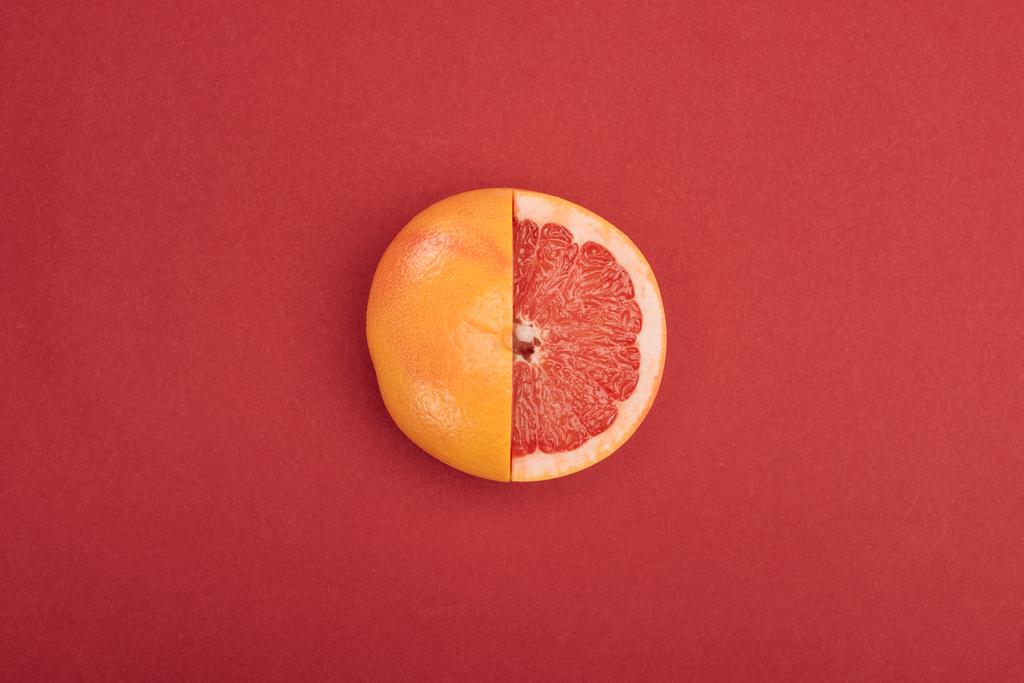 bovenaanzicht van verse rijpe gedeeltelijk knip grapefruit op rode achtergrond - Foto, afbeelding