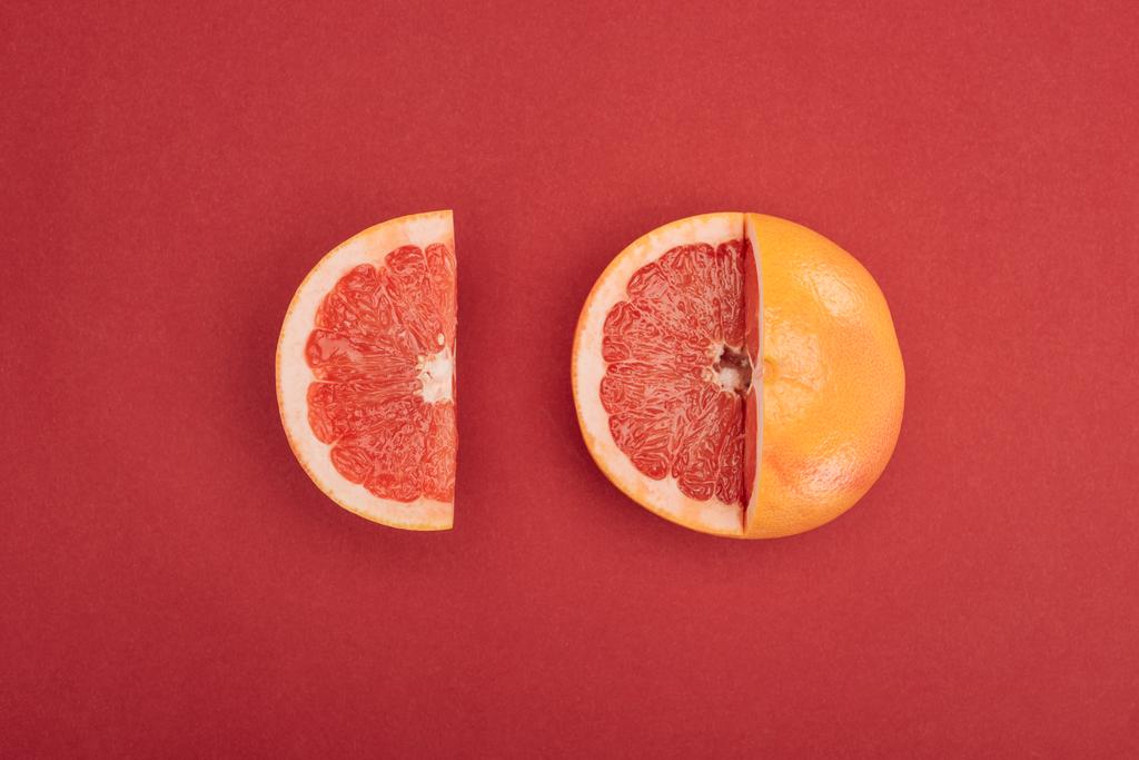 vista superior de la rodaja de pomelo y del pomelo parcialmente cortado sobre fondo rojo
 - Foto, Imagen