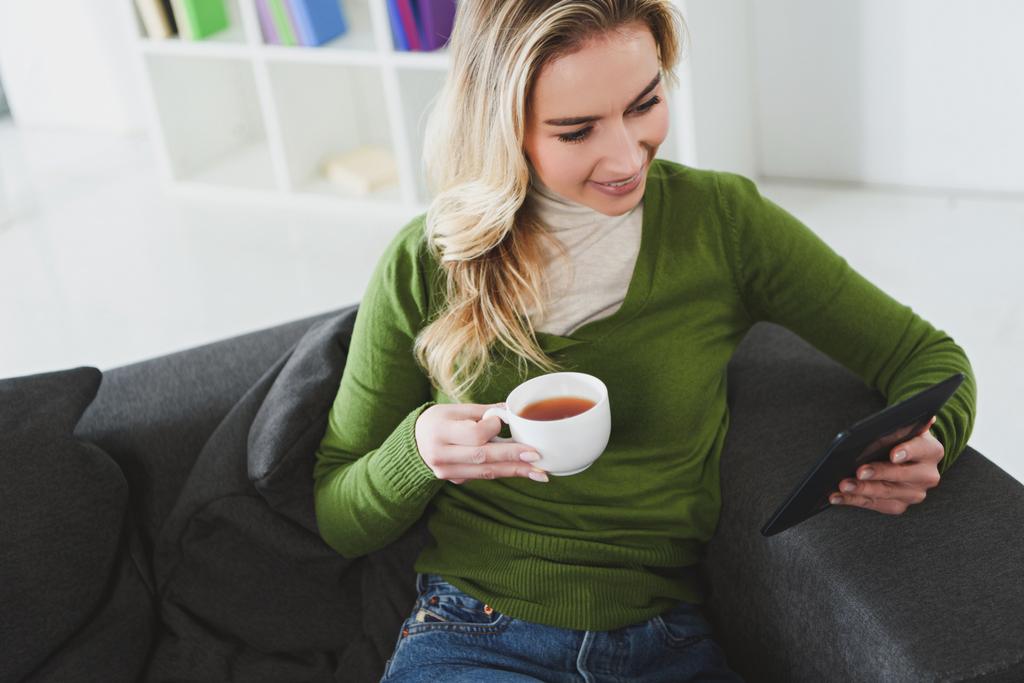 приваблива жінка тримає чашку з чаєм під час навчання з електронною книгою вдома
  - Фото, зображення