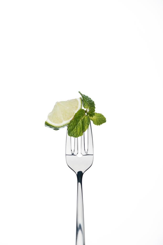 schijfje limoen en de munt laat op vork geïsoleerd op wit - Foto, afbeelding