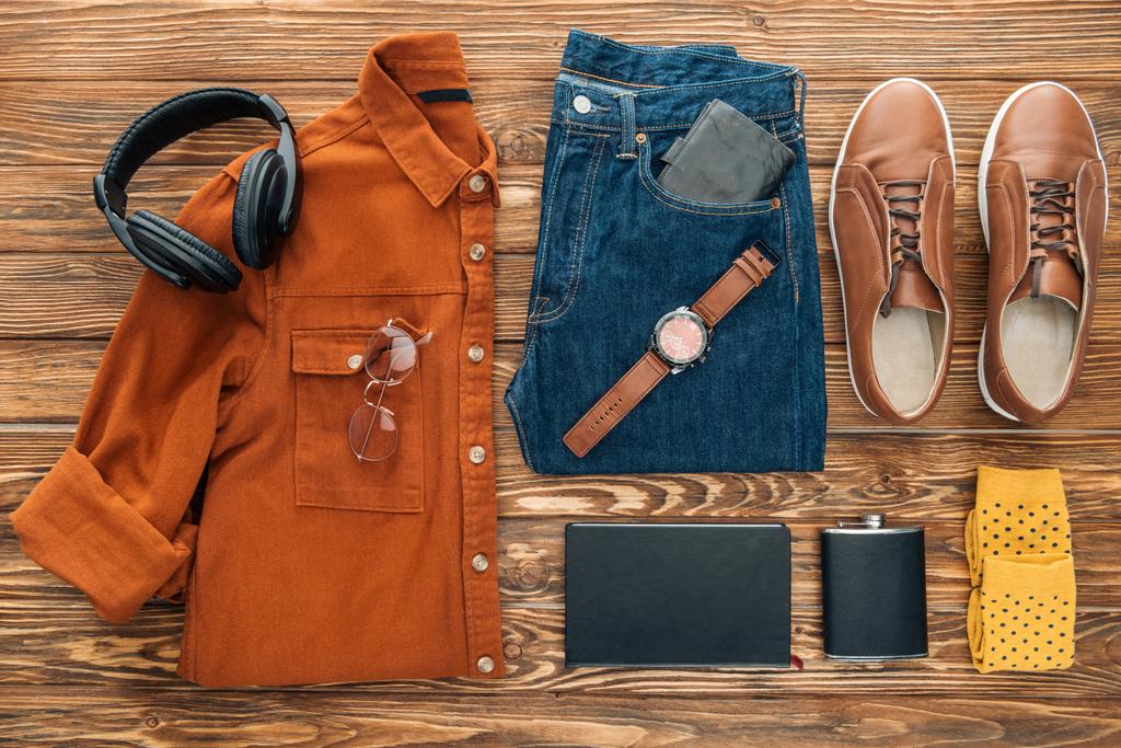 Asiento plano con auriculares, petaca y ropa masculina sobre fondo de madera
 - Foto, Imagen