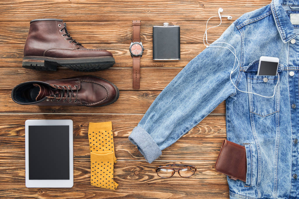 Colocação plana de botas, jaqueta de ganga e dispositivos digitais em fundo de madeira
 - Foto, Imagem