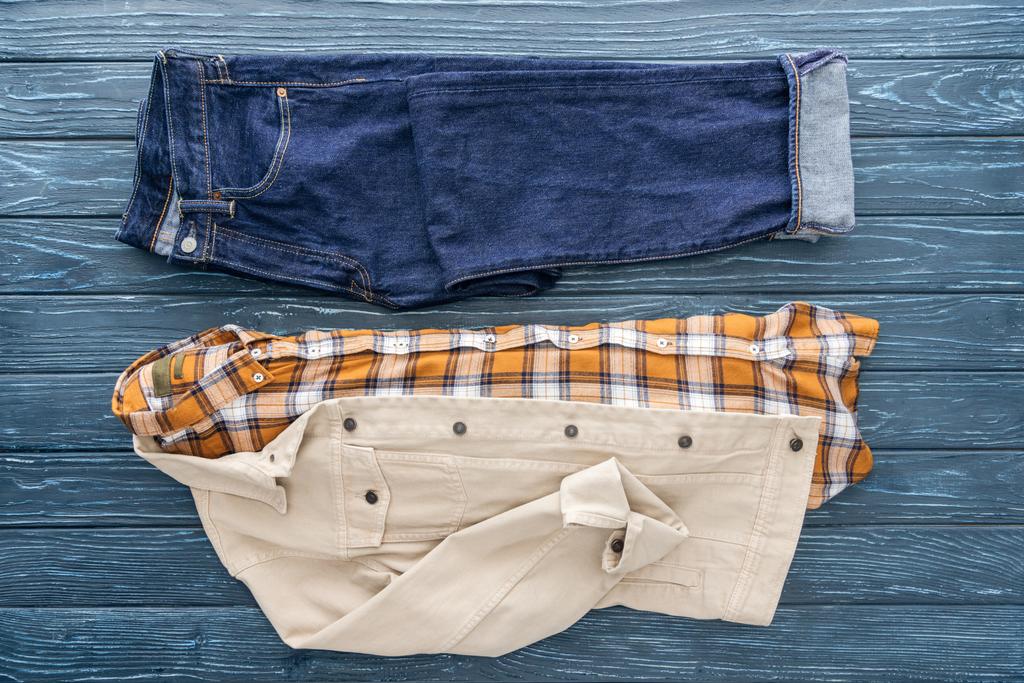Jeans, kariertes Hemd und Jacke auf hölzernem Hintergrund - Foto, Bild