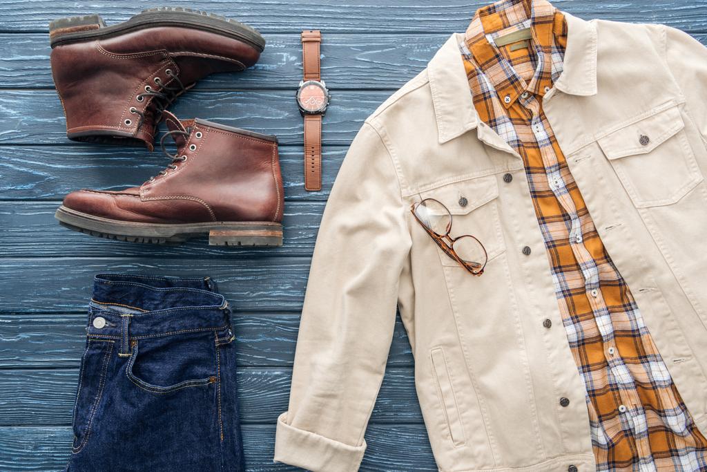Flat lay com jeans, camisa quadriculada e botas de couro em fundo de madeira
 - Foto, Imagem