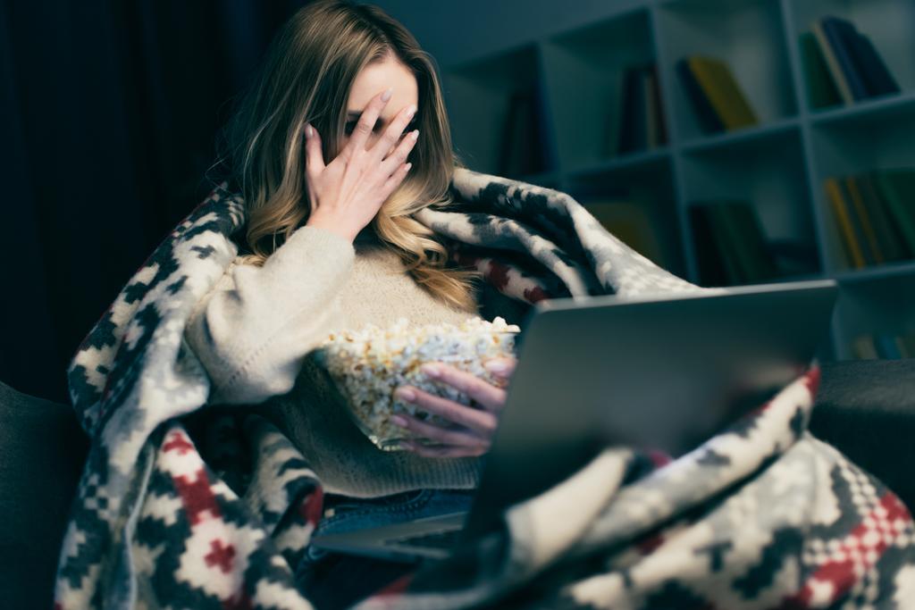 woman watching scary movie on laptop and covering face with hand  - Photo, Image
