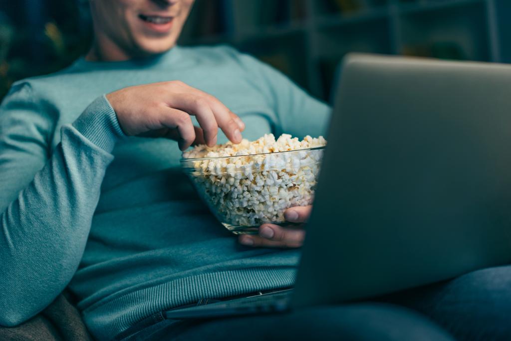 obcięty widok człowieka, oglądając film na laptopie i przytrzymując miska z popcornu  - Zdjęcie, obraz