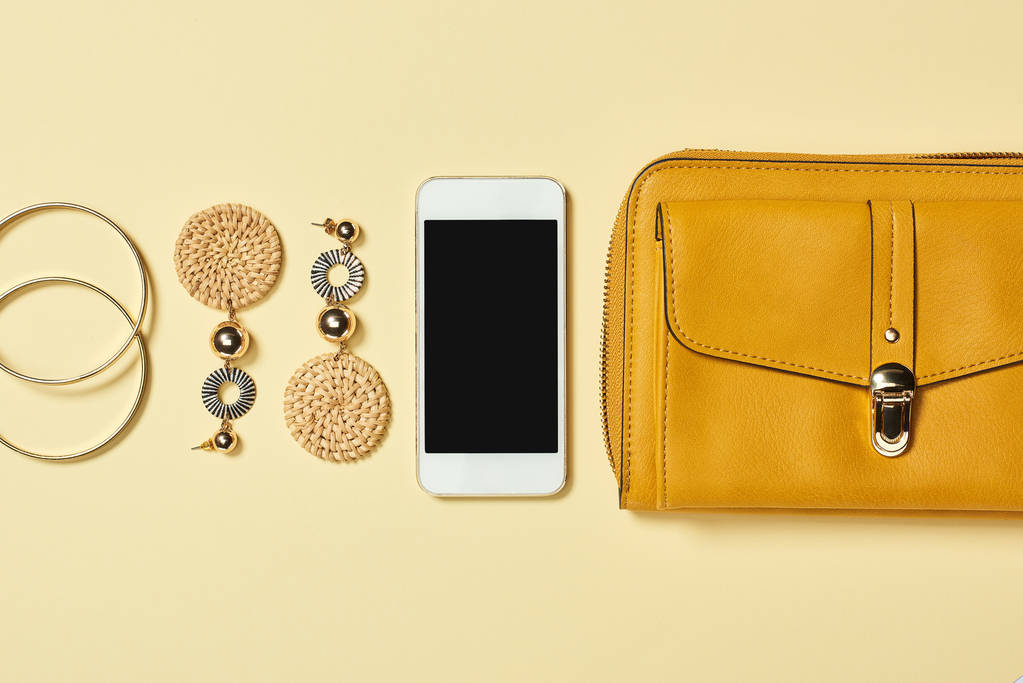 Bovenaanzicht van armbanden, oorbellen, smartphone en zak op gele achtergrond - Foto, afbeelding