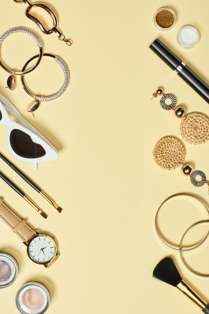 Horloge, zonnebril, oogschaduw, cosmetische penselen, armbanden, oorbellen en mascara op gele achtergrond - Foto, afbeelding