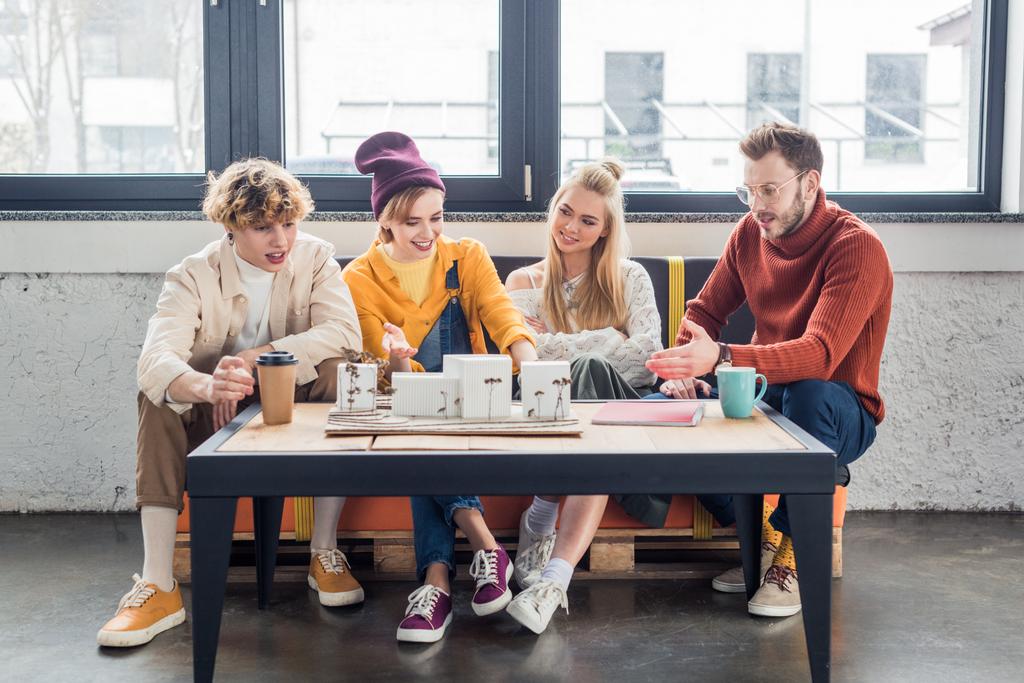 usmívající se skupina ženské a mužské architektů sedí u stolu a práci na house modelu v podkroví úřadu - Fotografie, Obrázek