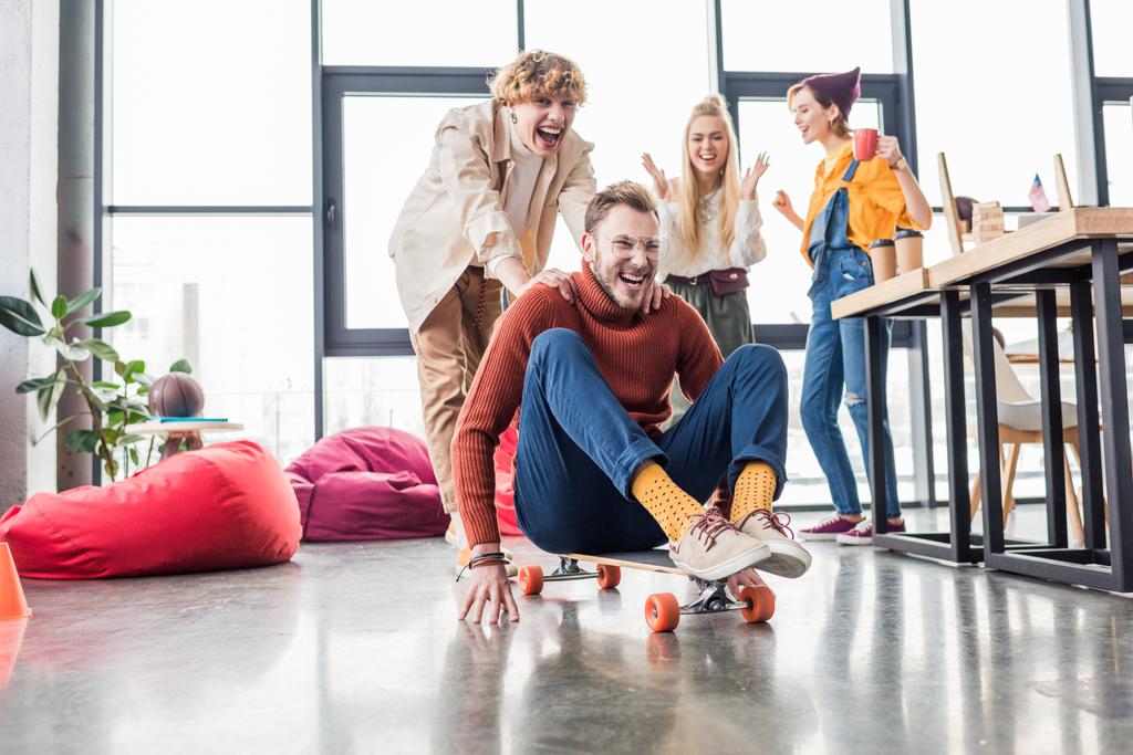 lächelnde Geschäftskollegen, die Spaß haben und im Loft-Büro Skateboard fahren - Foto, Bild