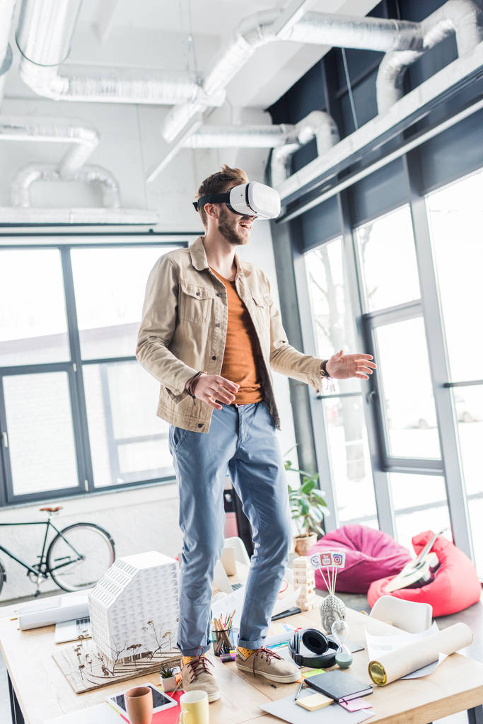 opgewonden mannelijke ontwerper gebaren met de handen terwijl het hebben van virtuele realiteit ervaring in loft kantoor - Foto, afbeelding