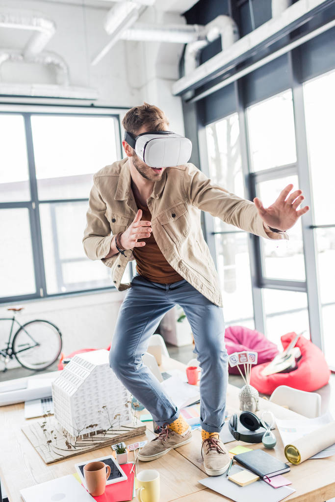yllättynyt mies arkkitehti eleiden kädet samalla ottaa virtuaalitodellisuus kokemus parvi toimistossa
 - Valokuva, kuva