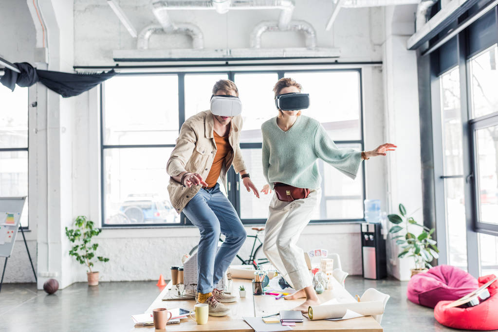 female and male architects wearing vr headset, gesturing with hands and having virtual reality experience in loft office - Photo, Image