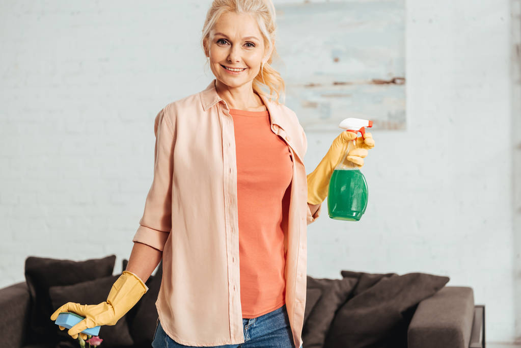 Gülümseyen kıdemli kadın holding temizleme spreyi ve sünger - Fotoğraf, Görsel
