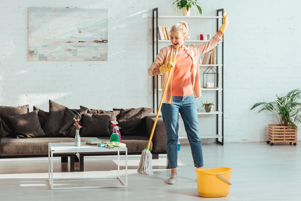 Full view of excited senior woman cleaning floor in living room - Photo, Image
