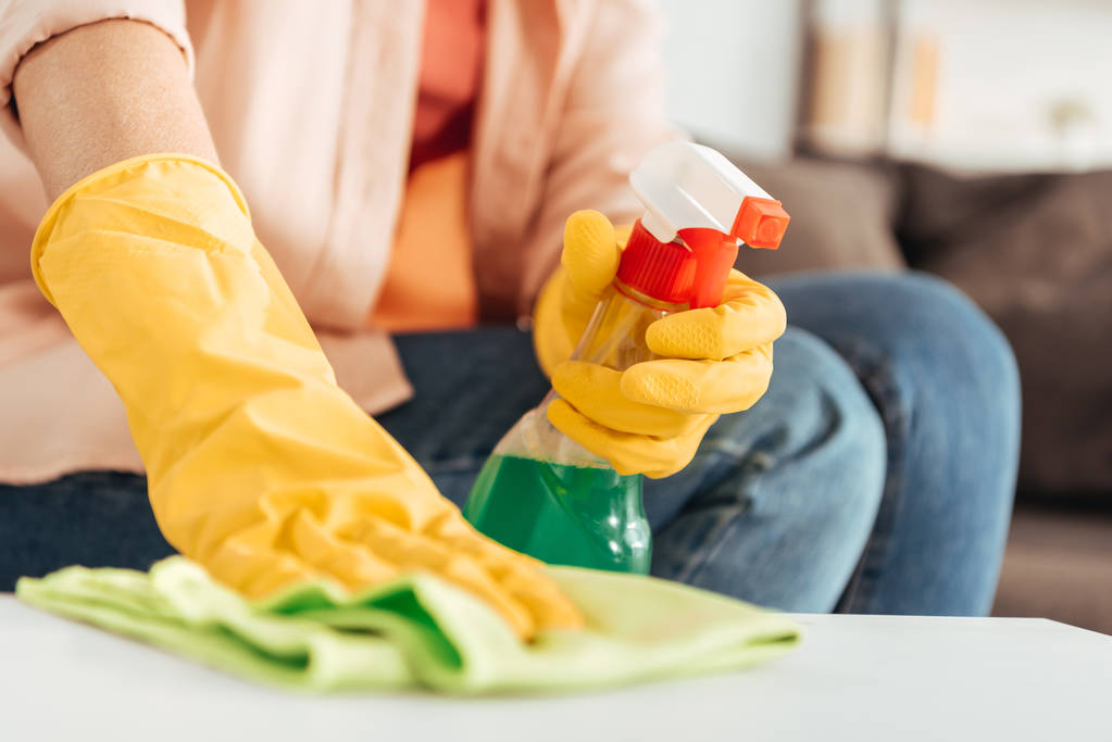 Teilansicht einer Frau in Gummihandschuhen, die Tisch mit Lappen putzt - Foto, Bild