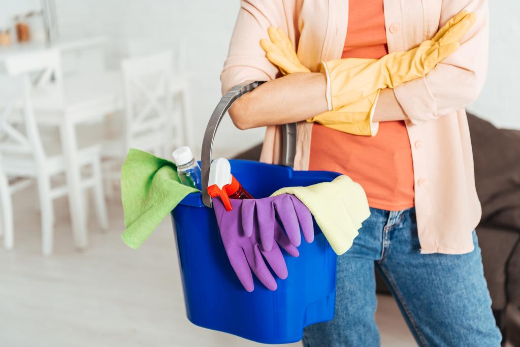 Обрезанный вид женщины в резиновых перчатках, держащей ведро с чистящими средствами
 - Фото, изображение