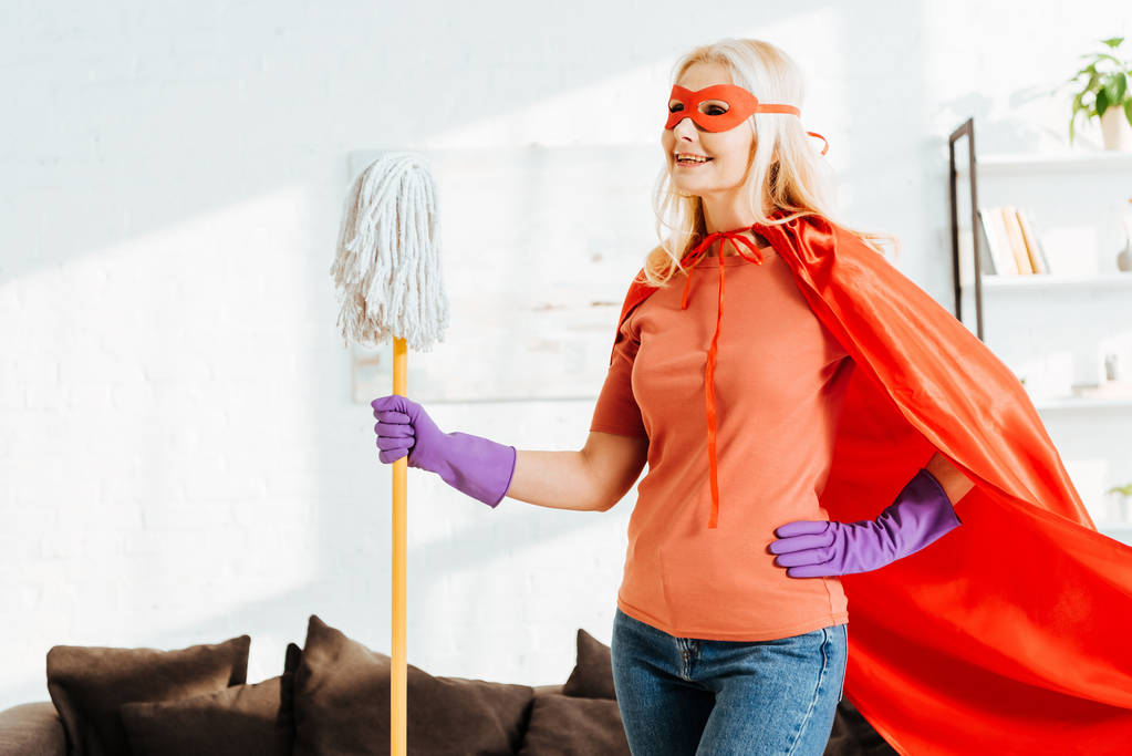 Mujer mayor alegre en traje de superhéroe posando con fregona
 - Foto, Imagen