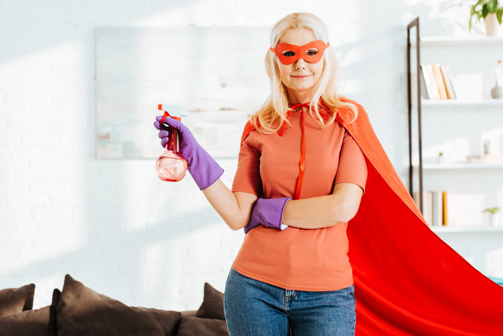 Selbstbewusste Seniorin im Superheldenkostüm und Gummihandschuhen mit Sprühflasche - Foto, Bild
