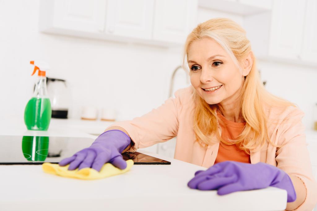 Sorrindo mulher sênior em luvas de borracha limpando fogão
 - Foto, Imagem