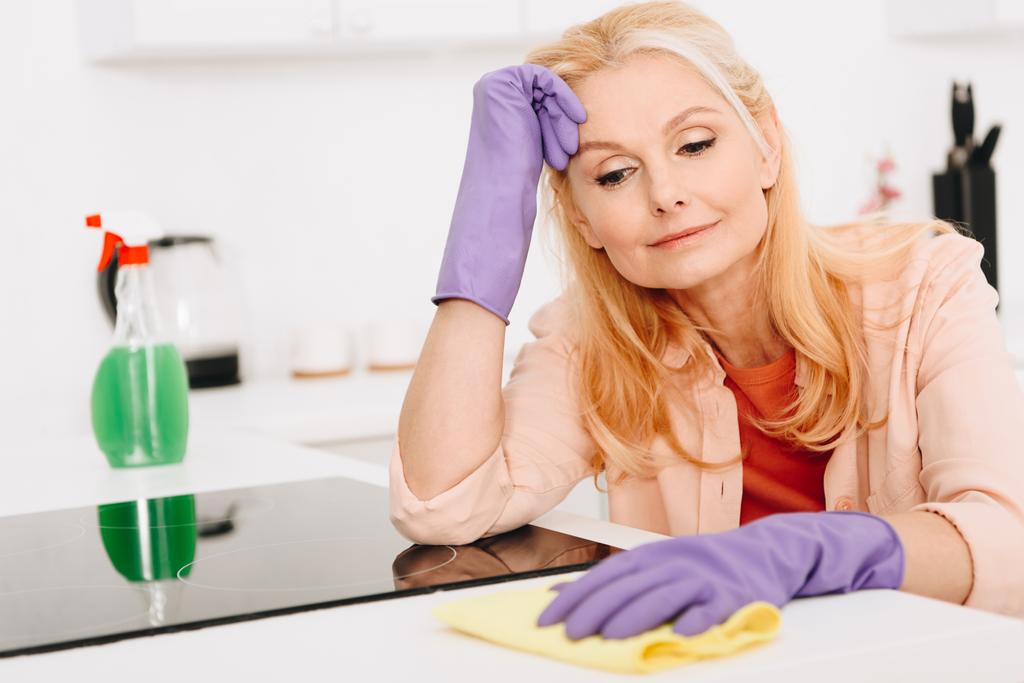 Moe senior vrouw in rubberen handschoenen keuken schoonmaken - Foto, afbeelding