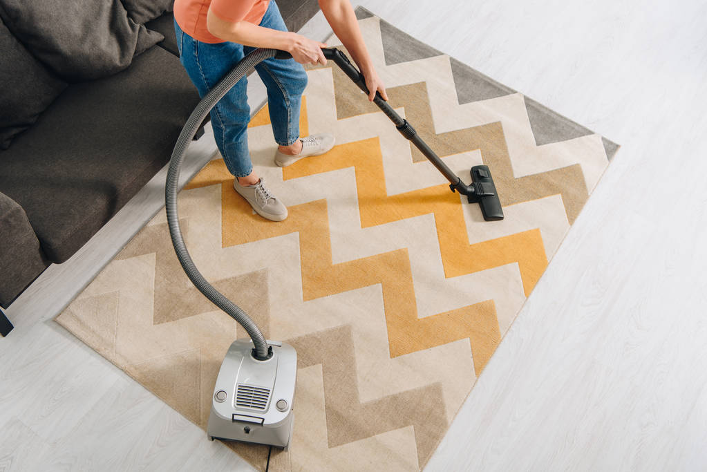 Ausgeschnittene Ansicht einer Frau, die Teppich mit Staubsauger reinigt - Foto, Bild