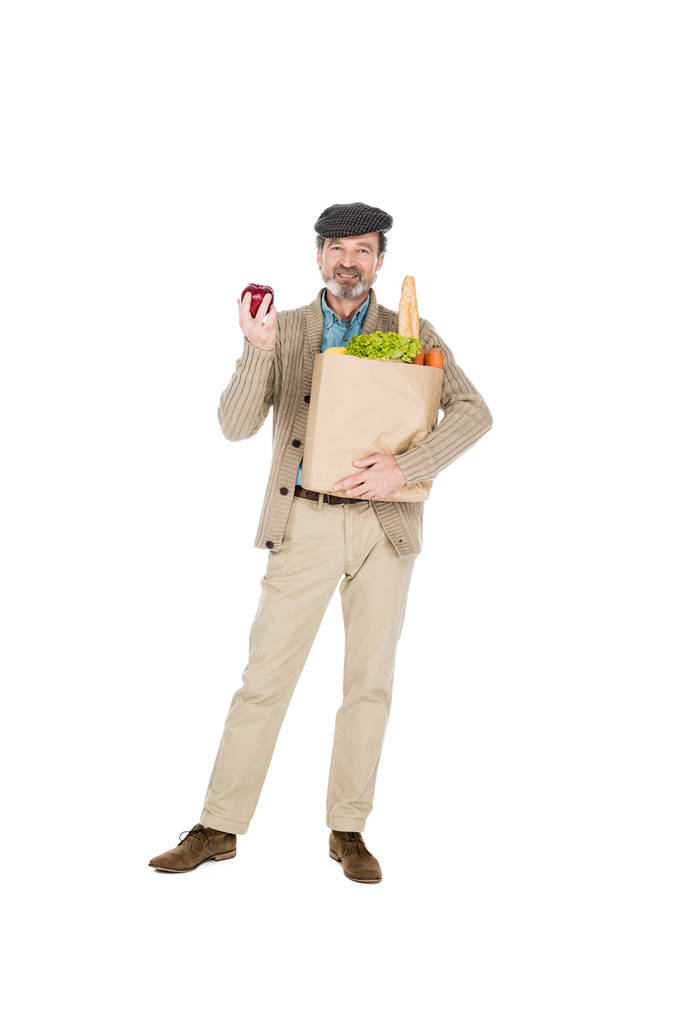 vrolijke senior man die apple en papieren tas met boodschappen geïsoleerd op wit - Foto, afbeelding