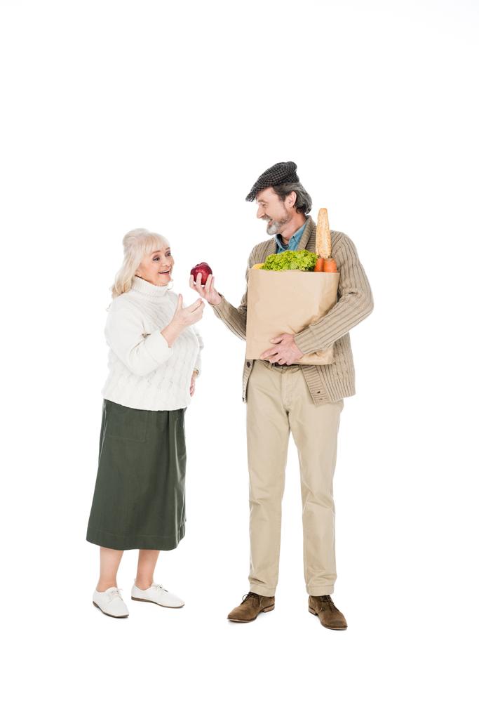 homme âgé joyeux montrant pomme à femme tout en tenant sac en papier avec épicerie isolé sur blanc
 - Photo, image