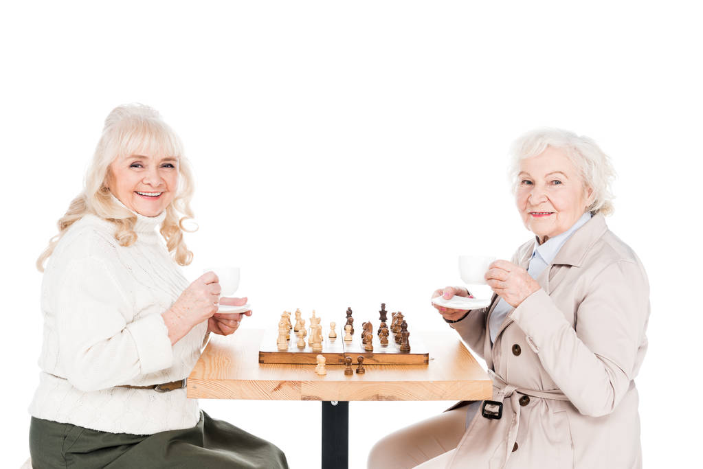 Rentnerinnen halten Tassen mit Getränken in der Hand, während sie Schach spielen - Foto, Bild