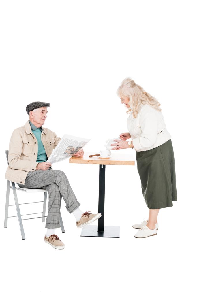 femme à la retraite regardant mari avec journal tout en versant le thé dans une tasse isolée sur blanc
  - Photo, image