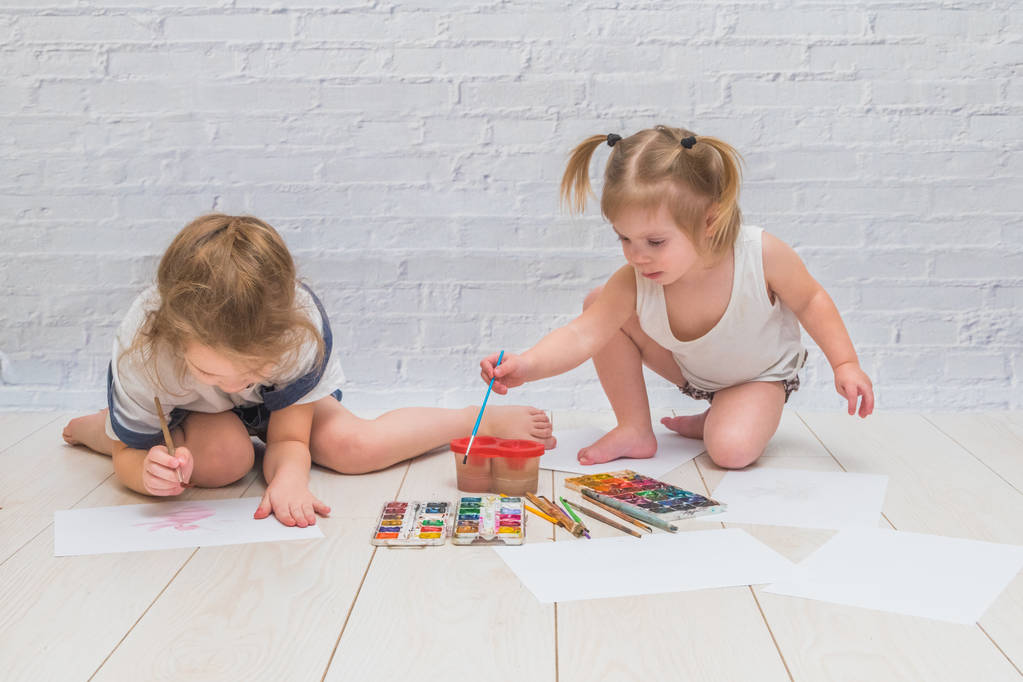 la fille, l'enfant dessine avec le pinceau et l'aquarelle, les peintures, sur la feuille du papier et les vêtements
 - Photo, image