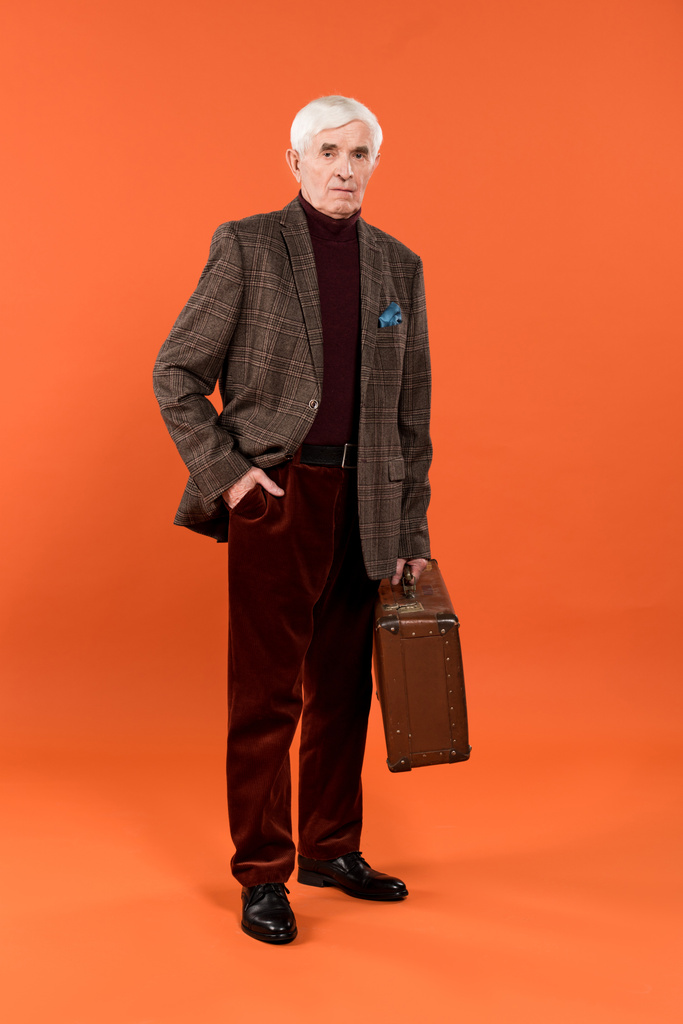 trendy senior man holding briefcase while standing on orange background - Photo, Image