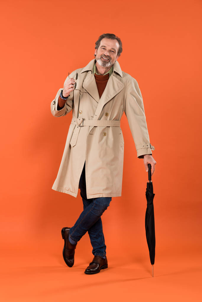 サングラスを押しながらオレンジ色の背景に傘の側に立って幸せの年配の男性  - 写真・画像