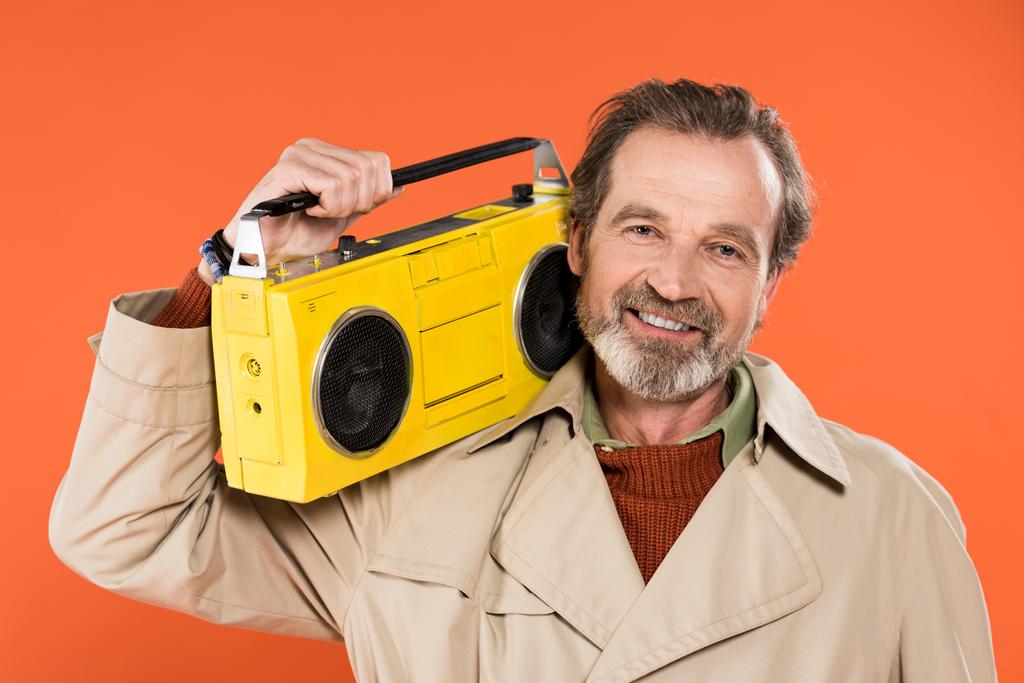 オレンジに分離された黄色のラジカセを保持している陽気な年配の男性 - 写真・画像