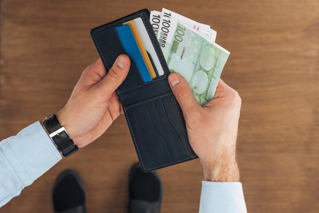 вид сверху на человека, вынимающего из бумажника с помощью кредитных карт евро банкноты на деревянном фоне
 - Фото, изображение