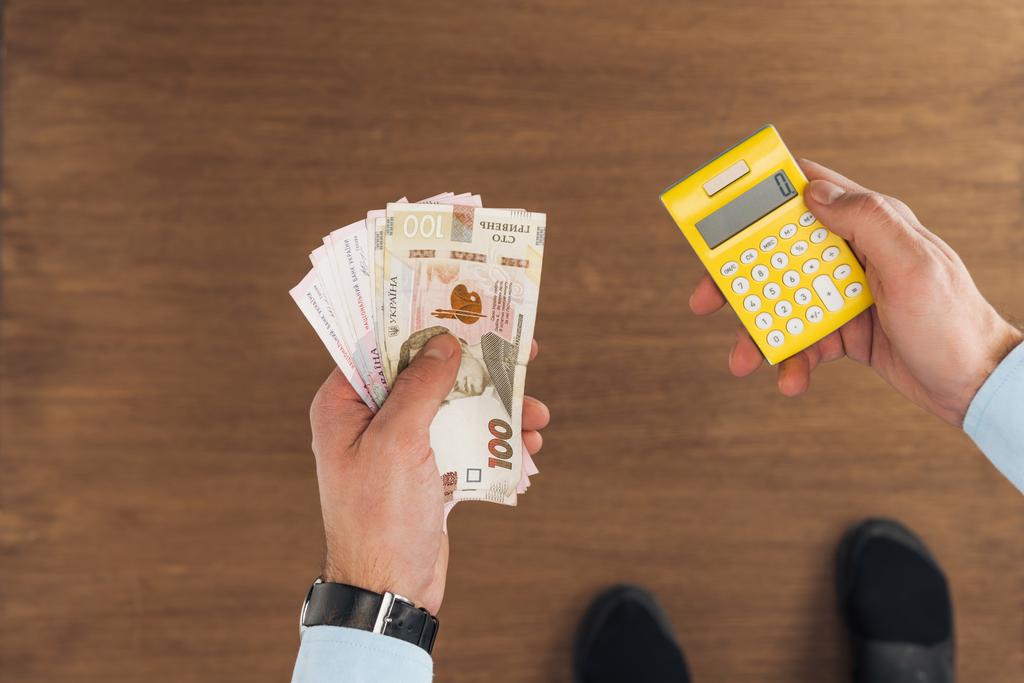 vue de dessus de l'homme tenant des billets de banque hryvnias et calculatrice sur fond en bois
 - Photo, image