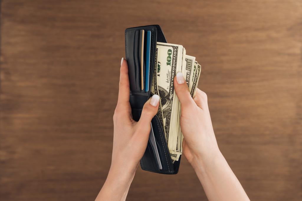 ylhäältä näkymä naisen laskemisesta dollareita seteleitä lompakossa puinen tausta
 - Valokuva, kuva