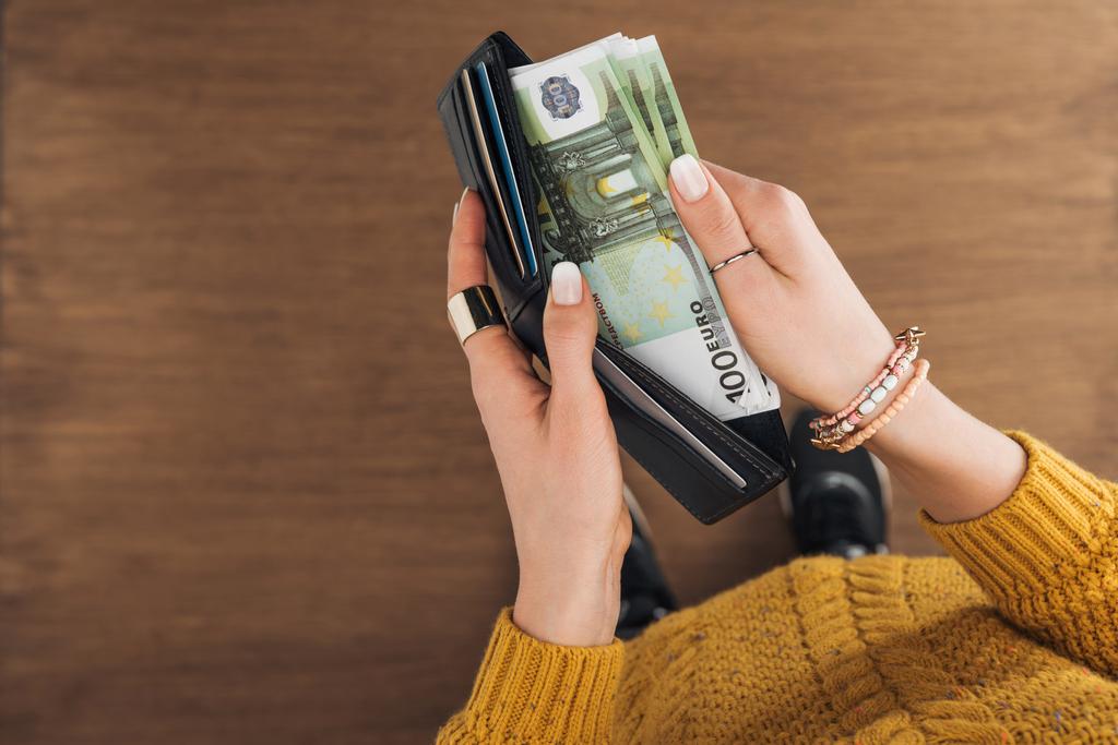 vista superior de la mujer que toma de la billetera billetes en euros sobre fondo de madera
 - Foto, Imagen