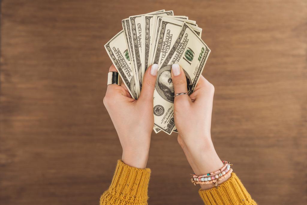 vista superior de la mujer sosteniendo billetes en dólares sobre fondo de madera
 - Foto, Imagen
