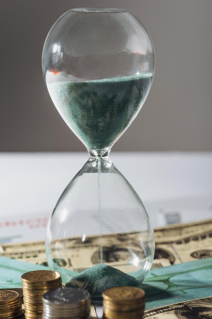Песочные часы и стопки монет на банкнотах с размытым фоном
 - Фото, изображение