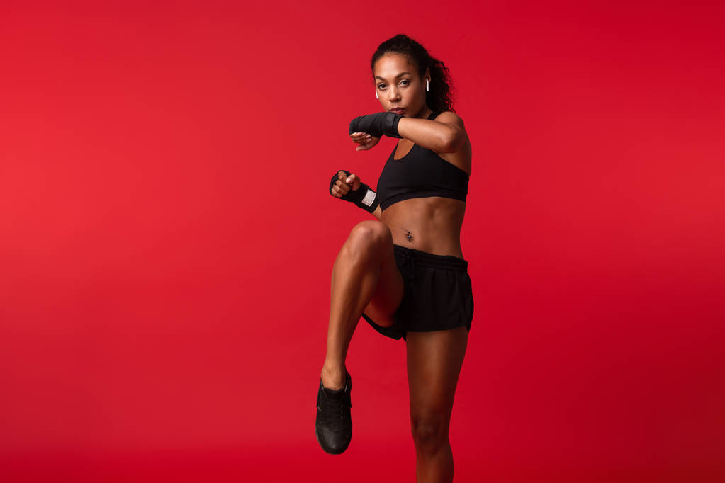 Εικόνα του σπορ αφρικανική αμερικανική γυναίκα σε μαύρα αθλητικά ενδύματα που φορώντας αθλητικά επίδεσμοι για τα χέρια που απομονώνονται σε κόκκινο φόντο - Φωτογραφία, εικόνα